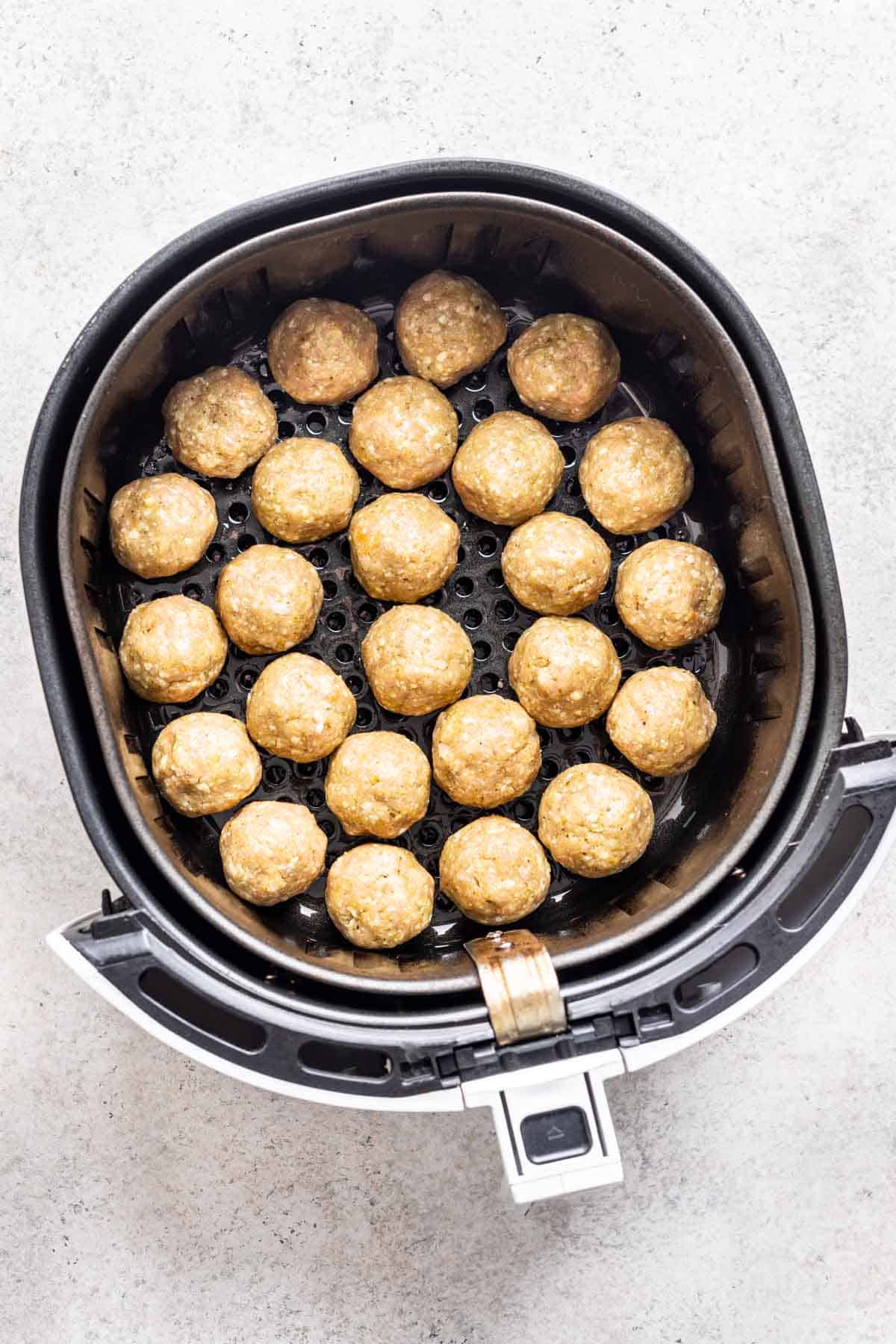 Raw chicken meatballs added to the basket of an air fryer.