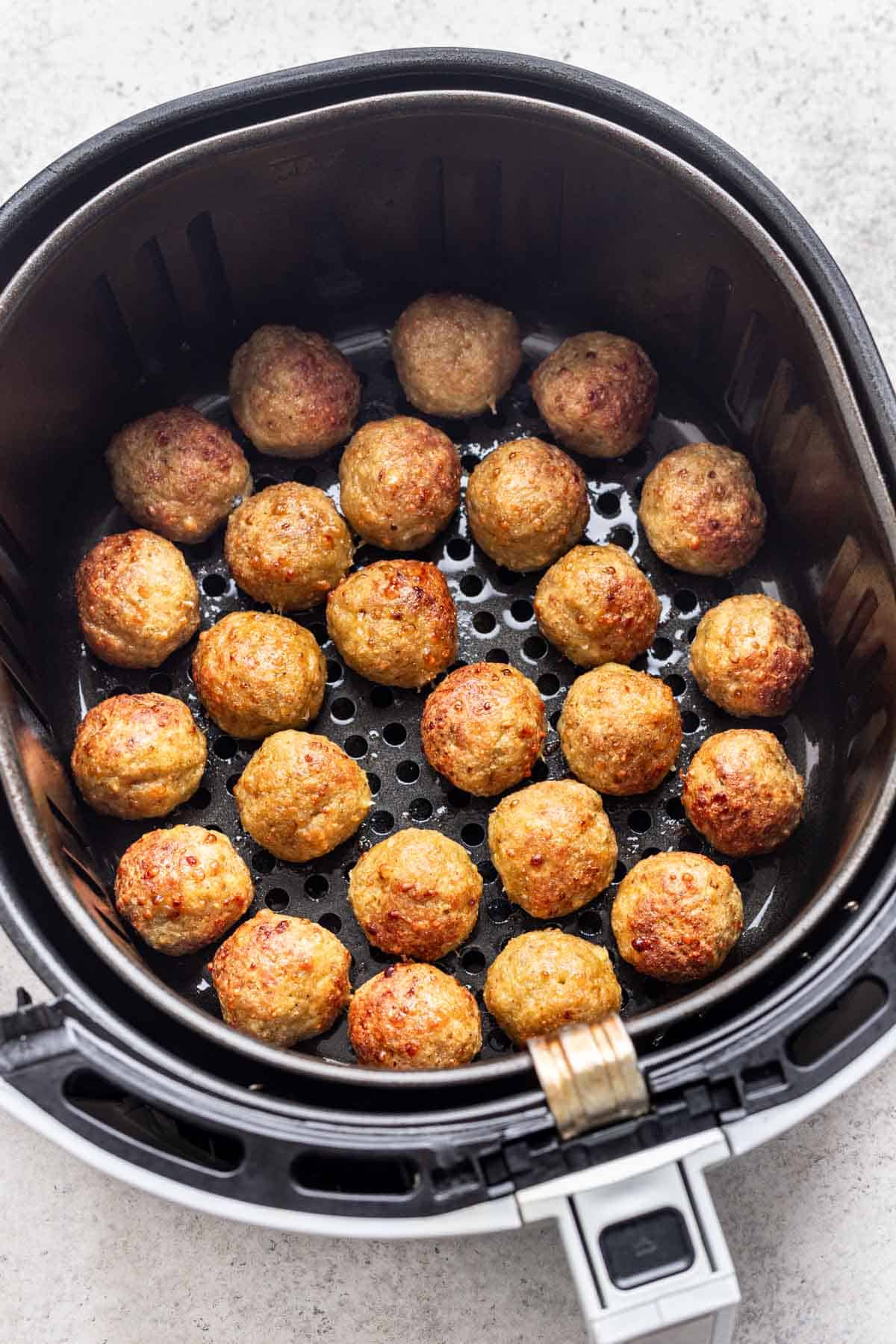 Golden brown chicken meatballs in an air fryer basket.