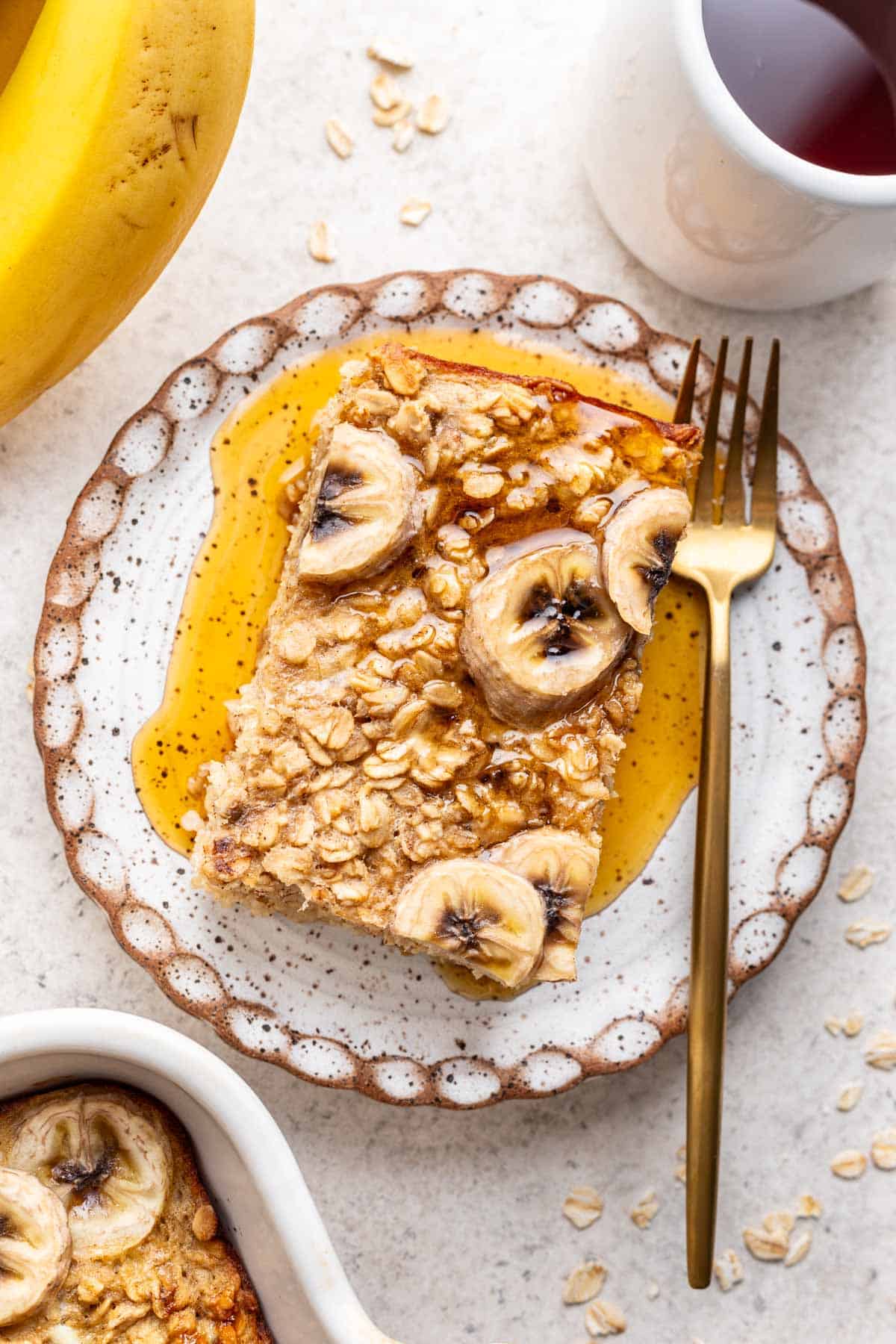 A slice of banana bread baked oats on a plate with maple syrup on top.
