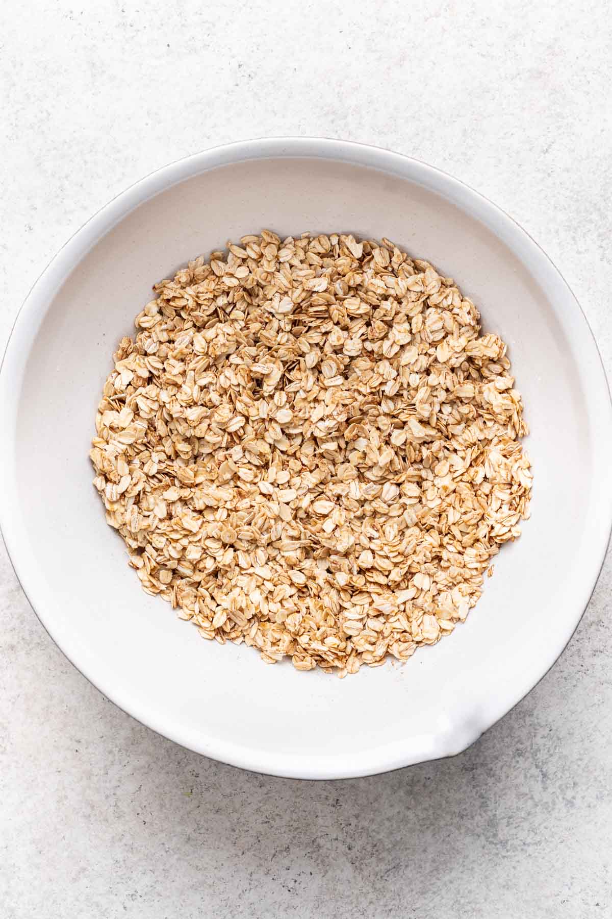 Oats, baking powder, cinnamon, and salt mixed together with coconut oil in a large bowl.