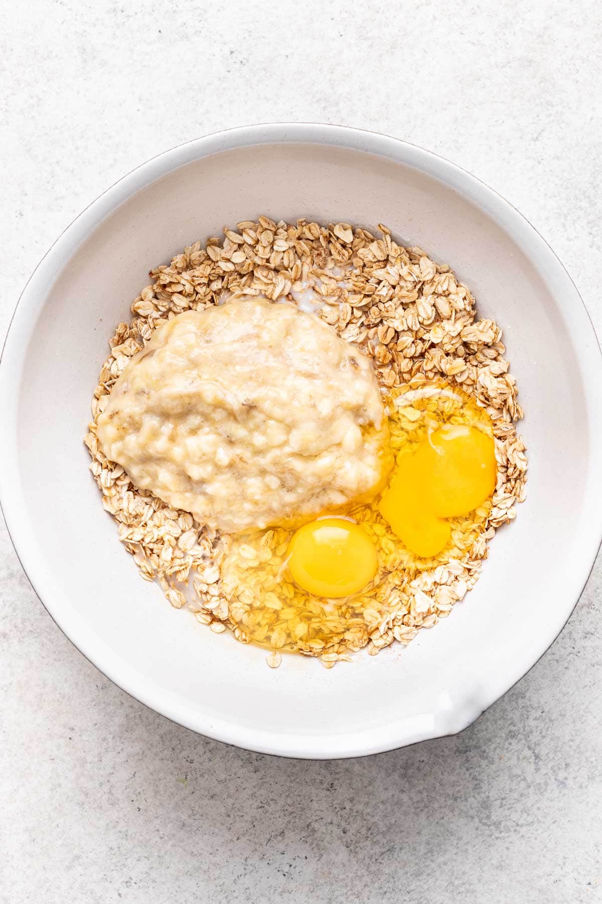 Wet ingredients added to the oats in a large mixing bowl.