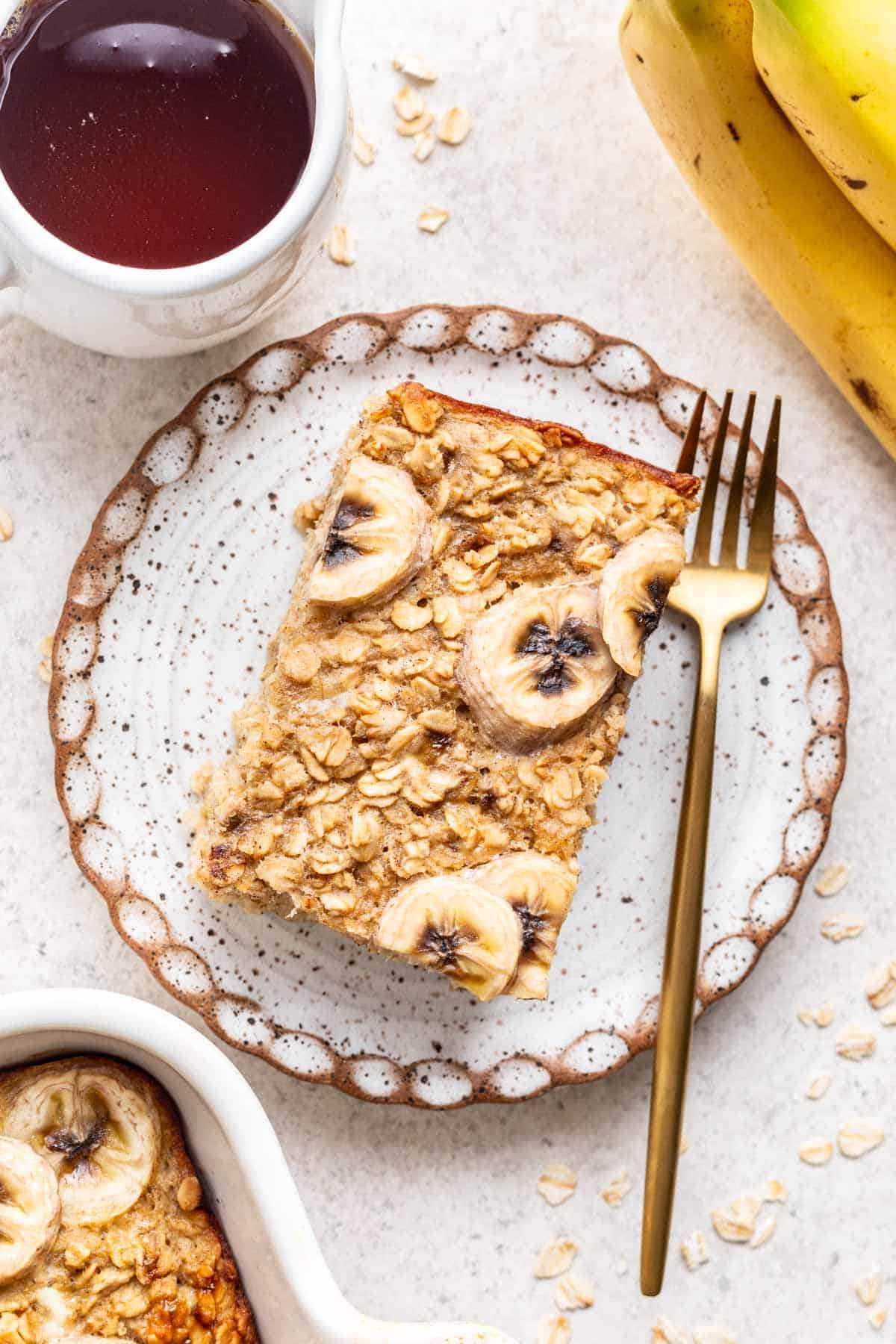 A slice of banana baked oats on a white plate with a gold fork.