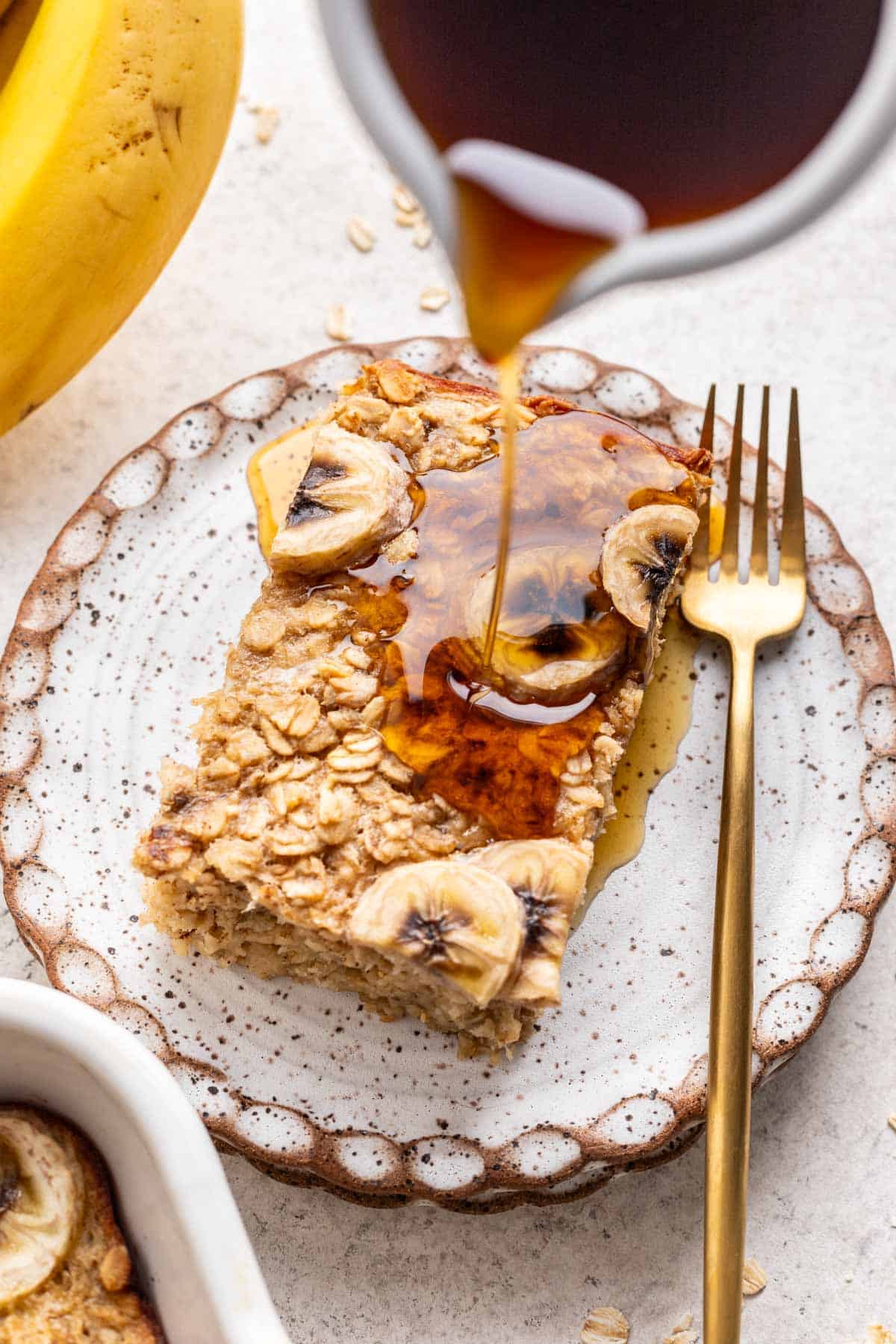 A carafe pouring maple syrup on top of banana bread baked oats.