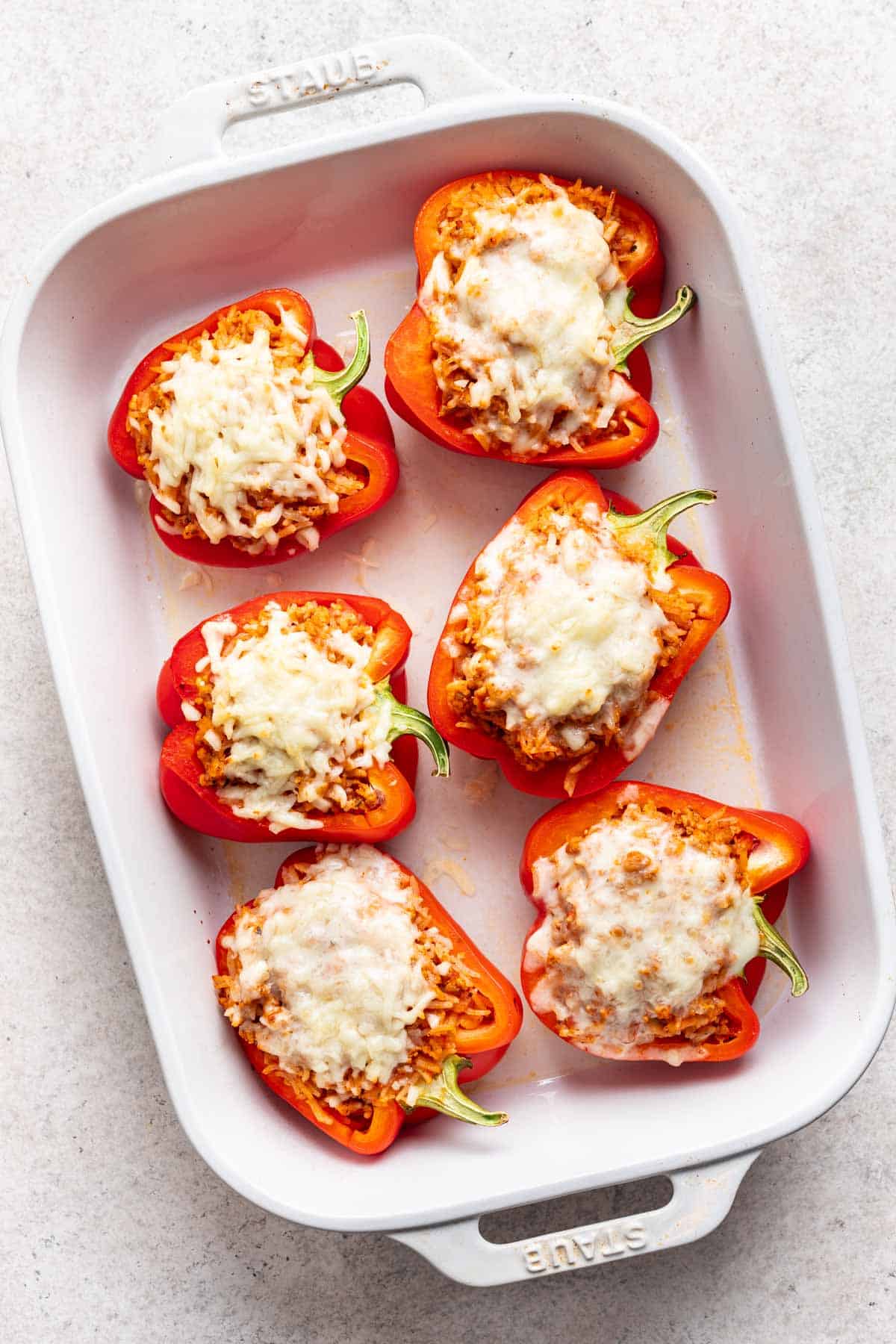 Melted mozzarella cheese on top of ground chicken stuffed peppers in a white baking dish.