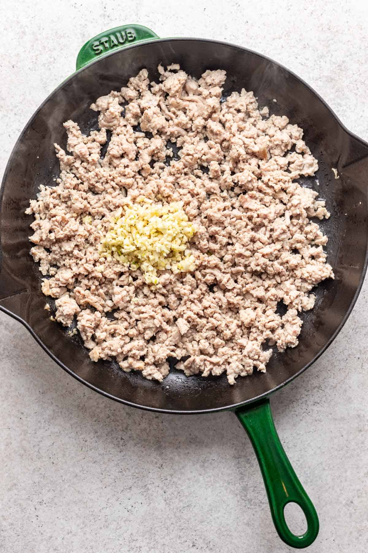 Minced garlic added to ground chicken in a skillet.