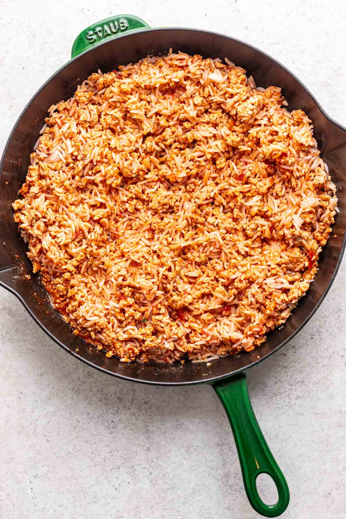 Rice and parmesan cheese added to the skillet with the ground chicken.