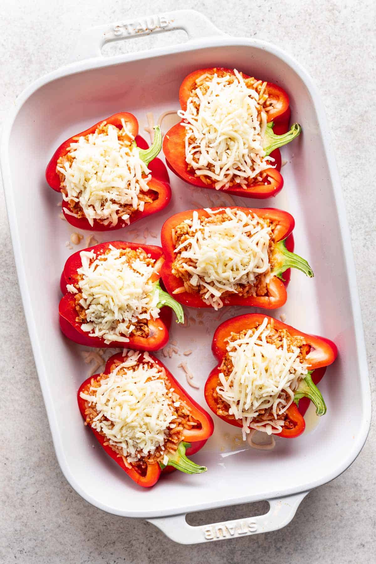 Ground chicken filling added to bell peppers, then topped with shredded mozzarella cheese, in a baking dish.