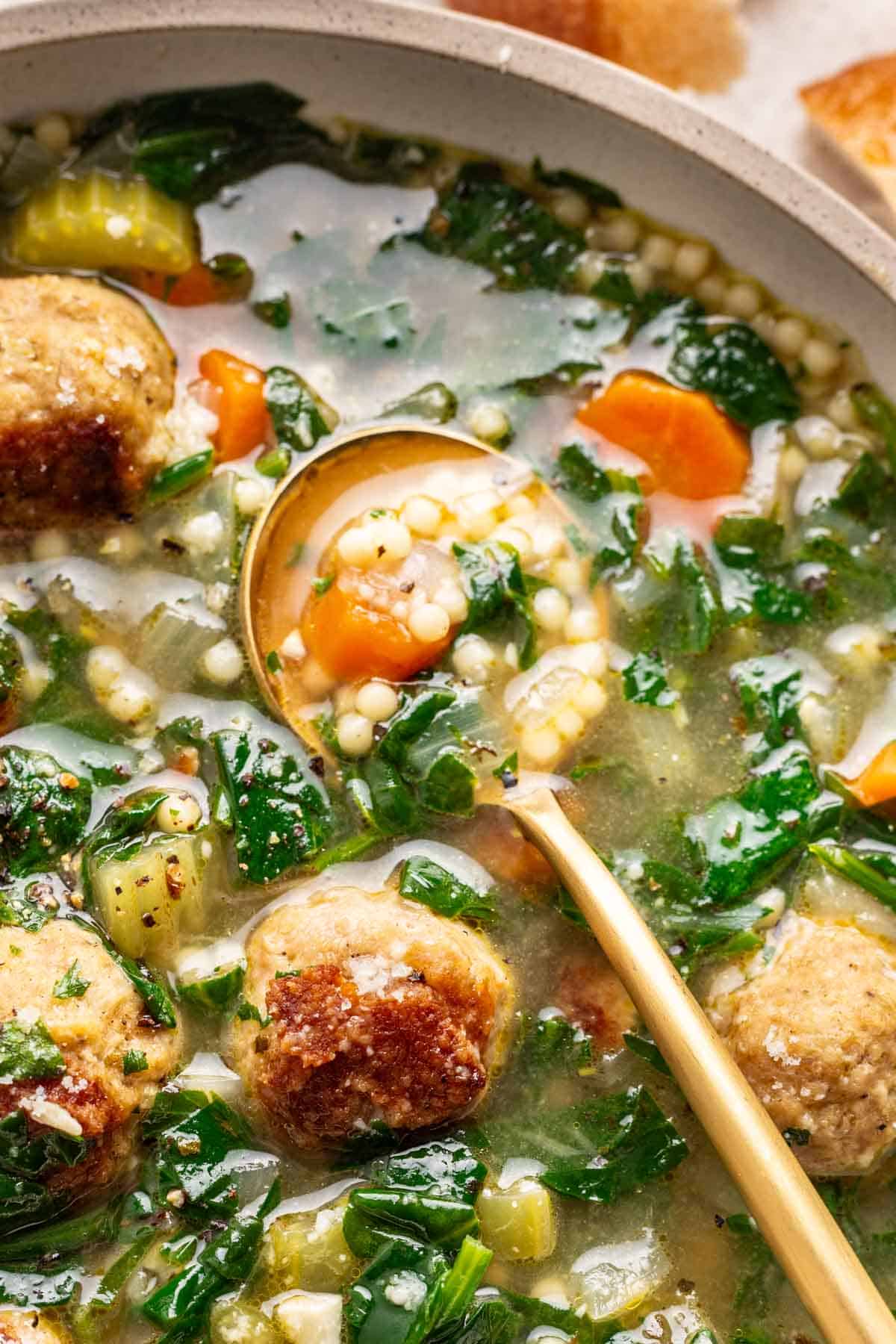 A spoon scooping Italian wedding soup out of a bowl.