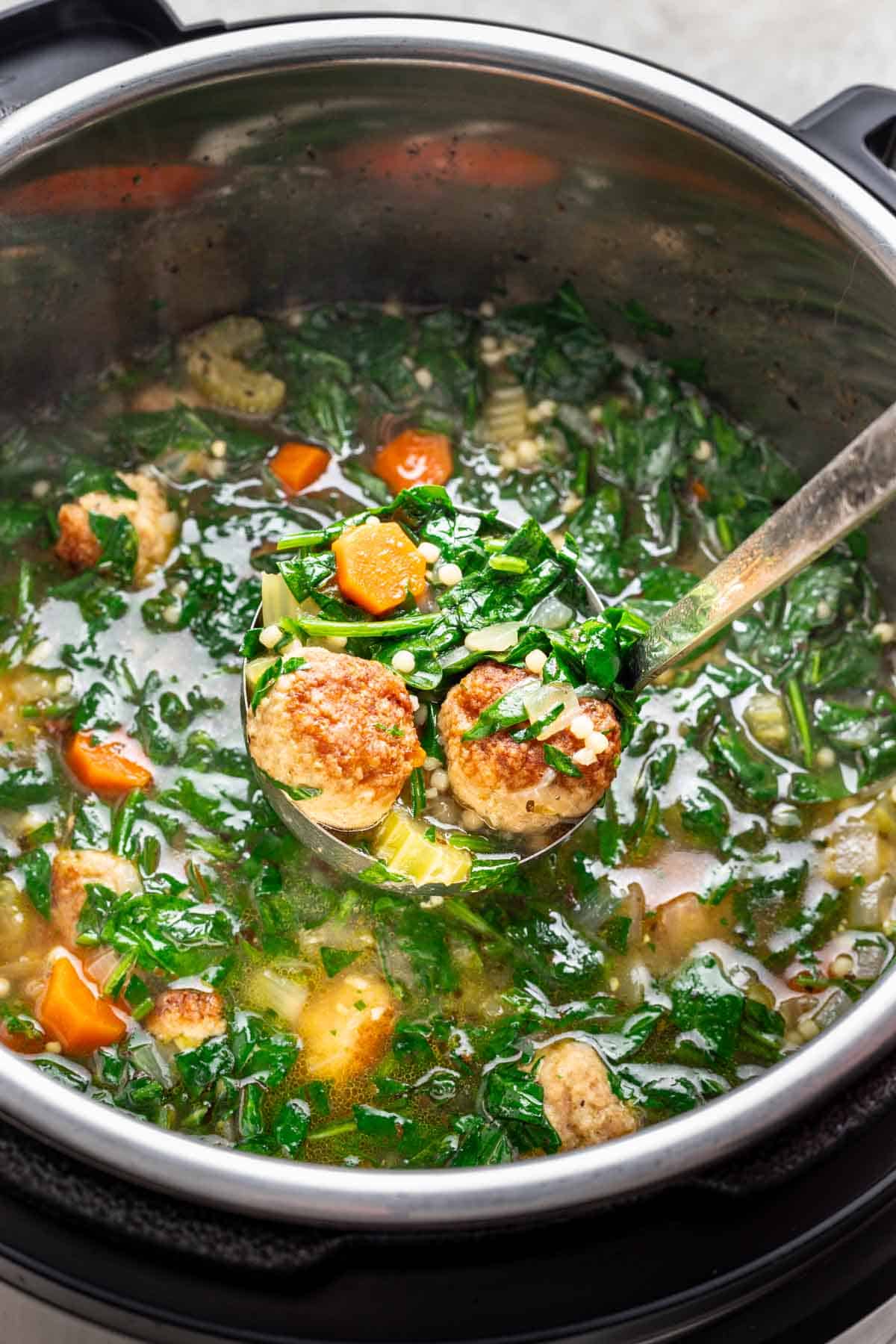 A ladle scooping meatballs and italian wedding soup out of an instant pot.