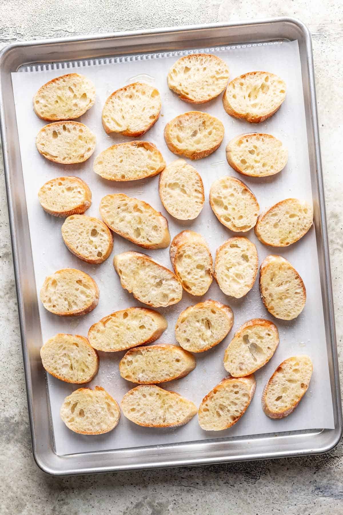 Sliced french baguette on a baking sheet before baking.