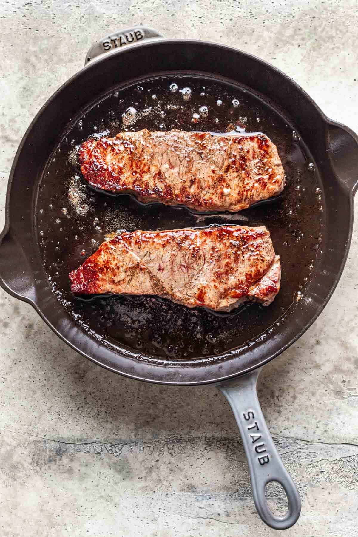 Cooked strip steaks in a skillet.