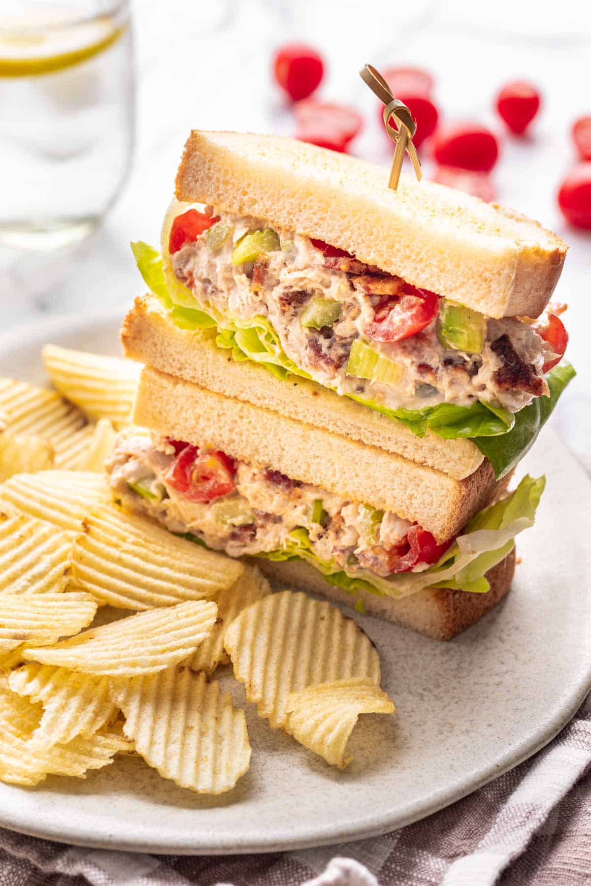 An avocado BLT chicken salad sandwich on a plate with ruffled potato chips.