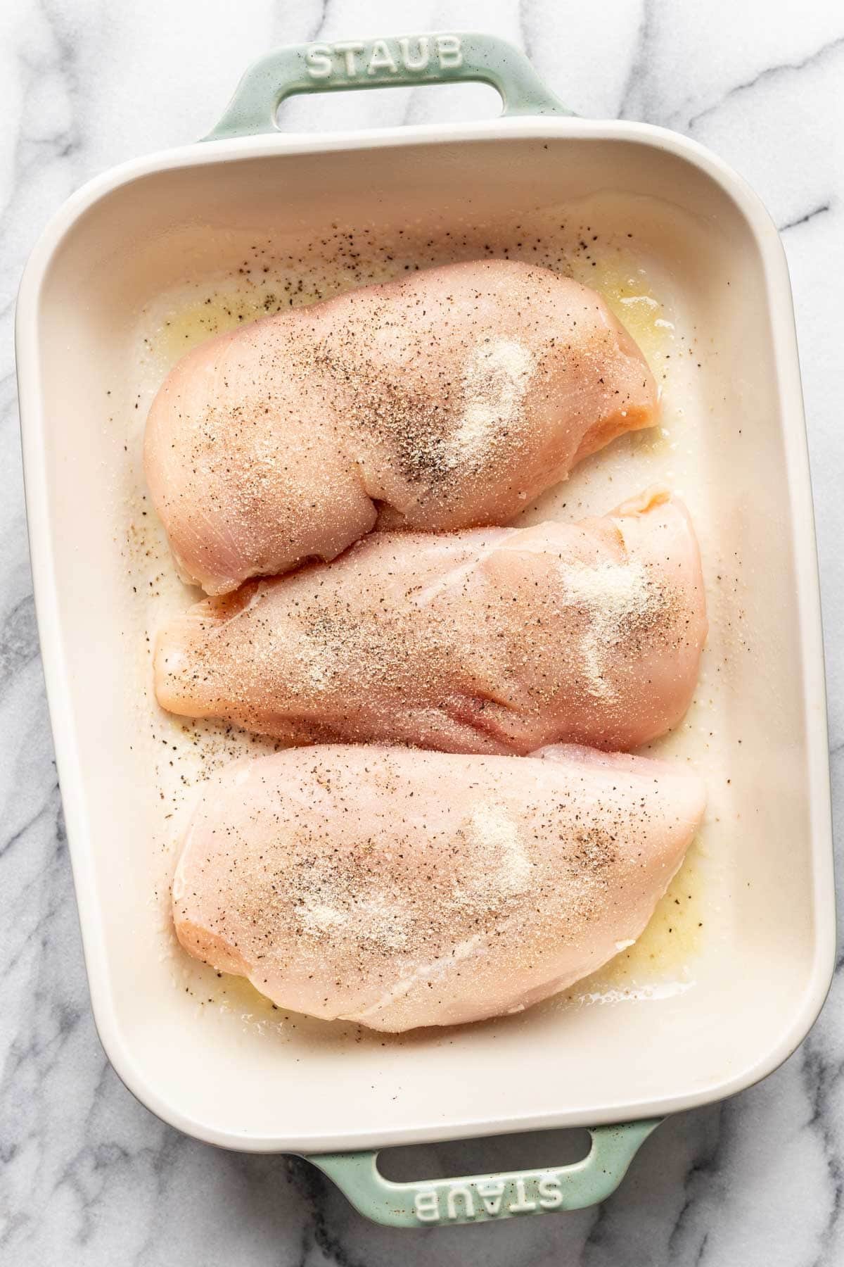 Raw chicken breasts in a baking dish, seasoned with salt, pepper, and onion powder.