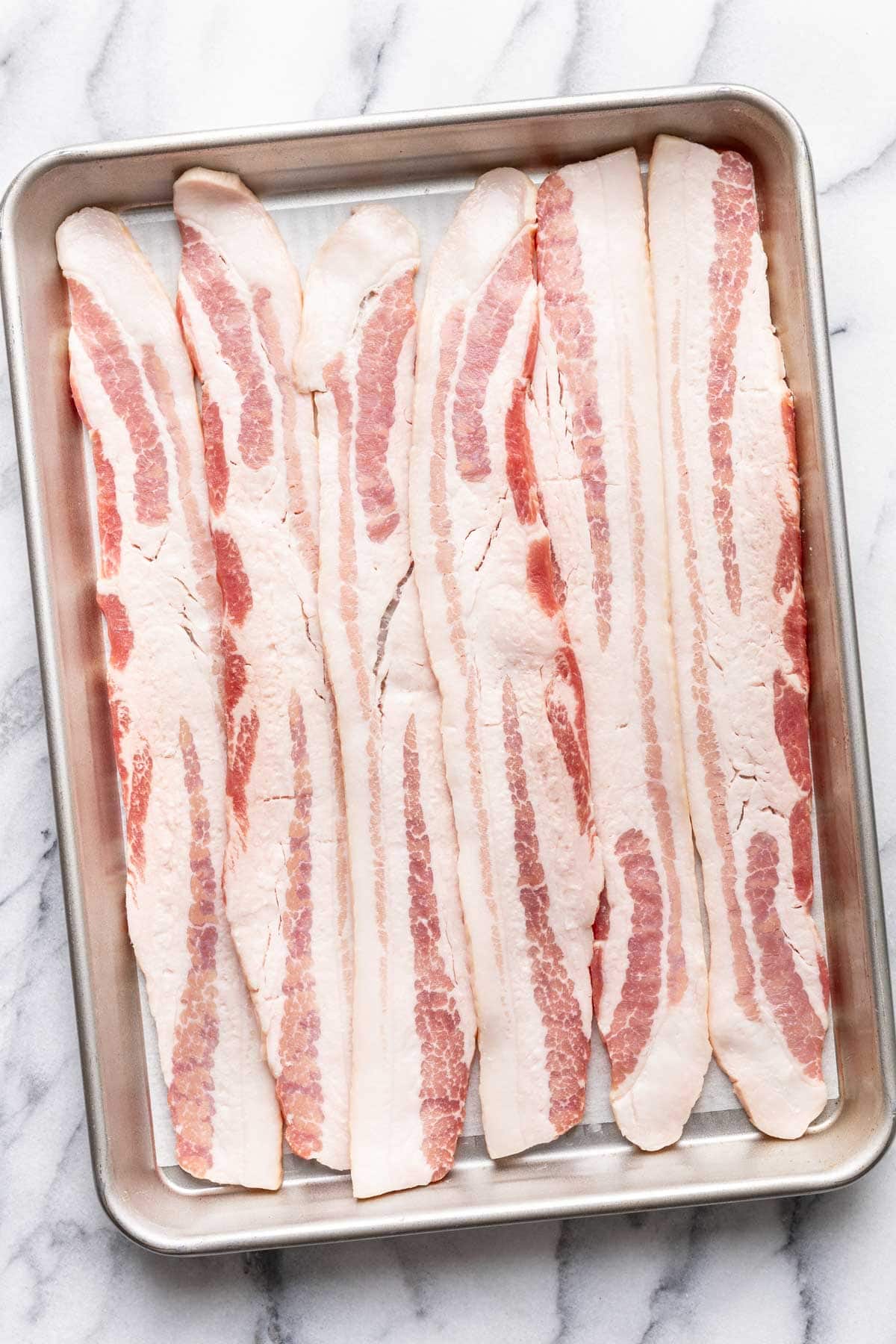 Uncooked bacon on a baking sheet.