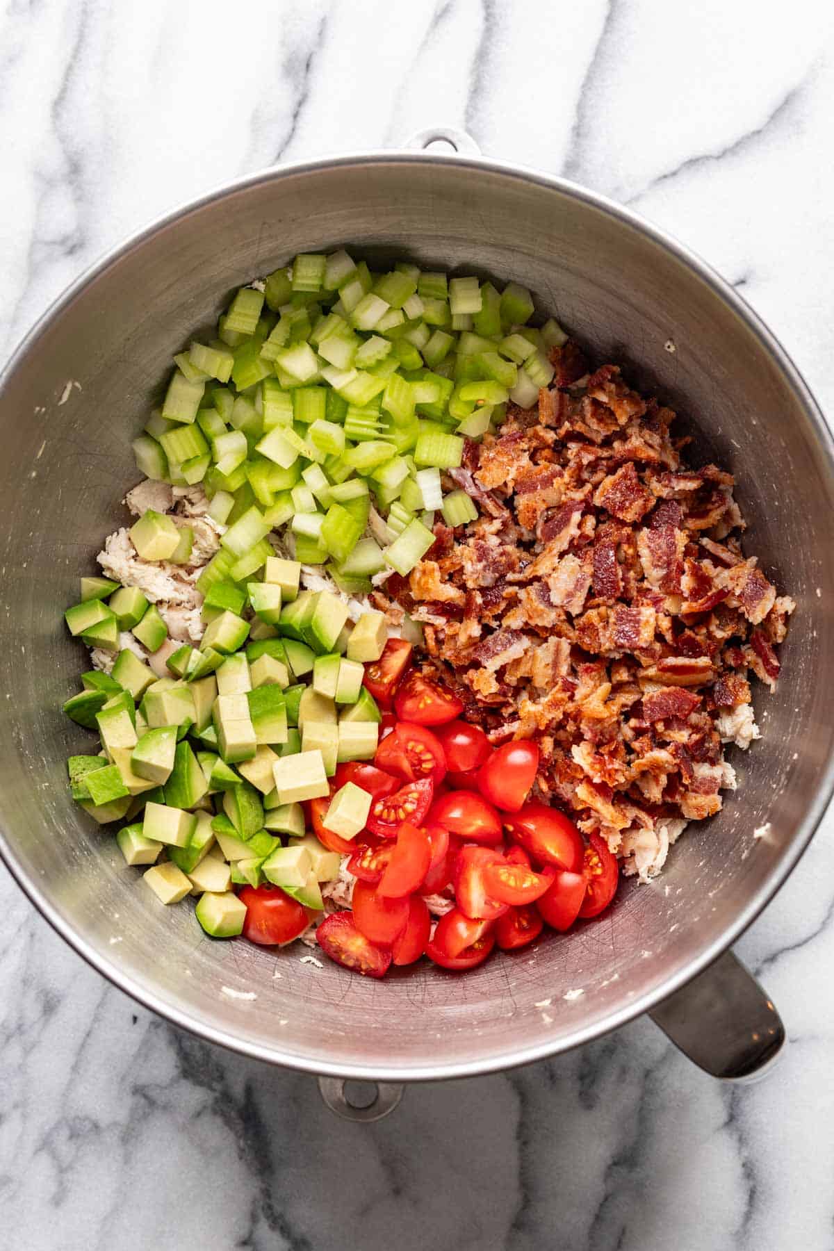 Bacon, tomatoes, celery, and avocado added to the shredded chicken in the bowl.