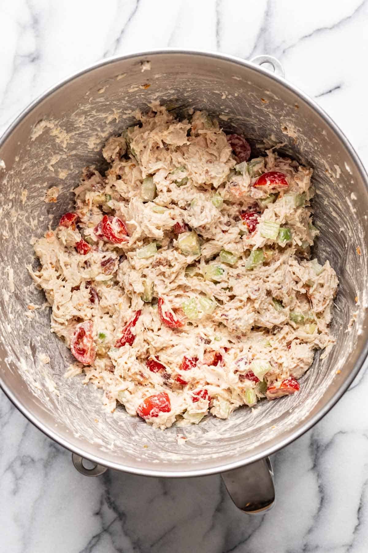 Mayonnaise and dijon mixed into the chicken salad in a mixing bowl.