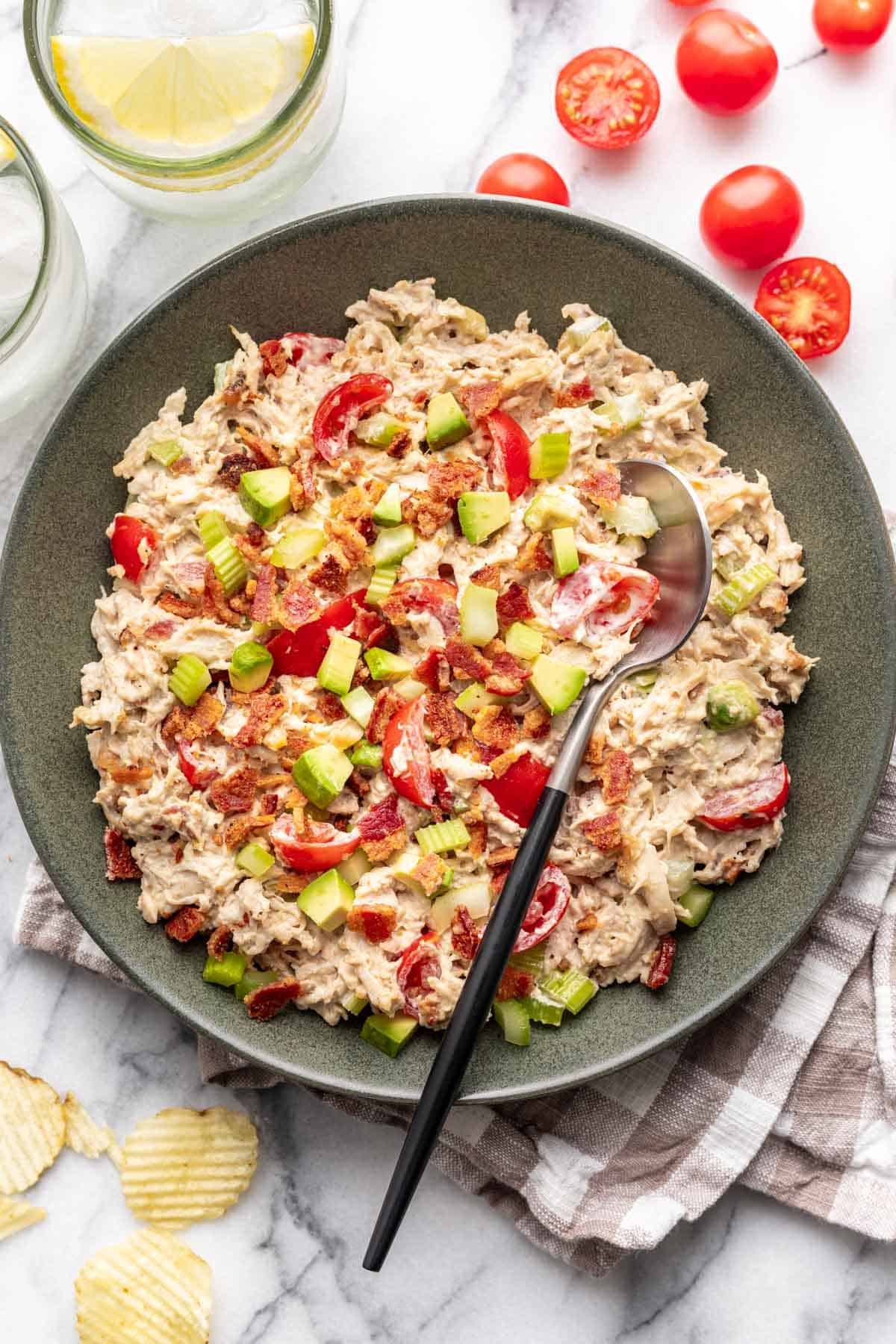 Avocado BLT chicken salad in a green bowl with a silver serving spoon.