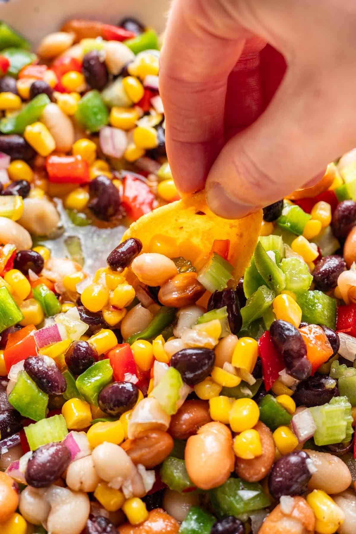 A tortilla chip scooping bean, corn, and veggie dip, showing the apple cider dressing in the bowl.