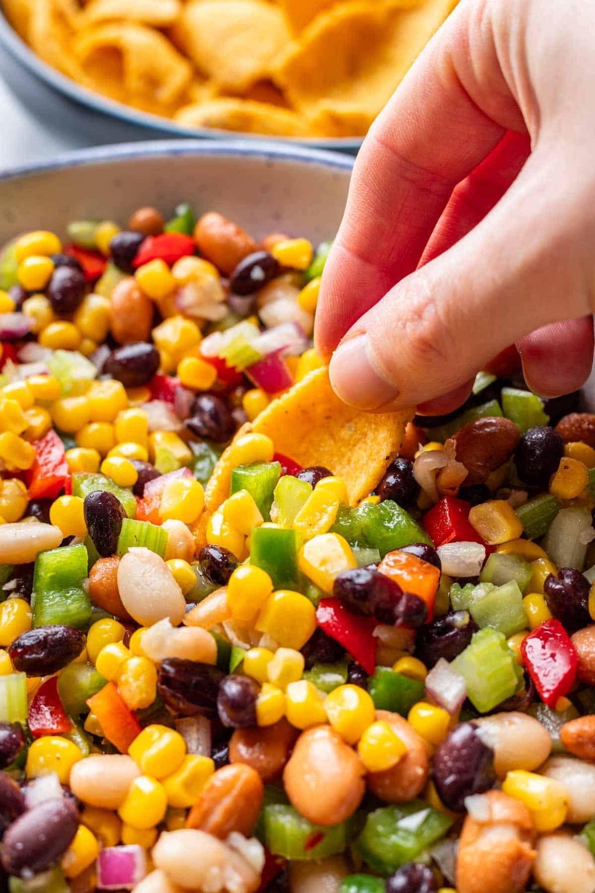 A hand using a tortilla chip to scoop up this homemade cowboy caviar.