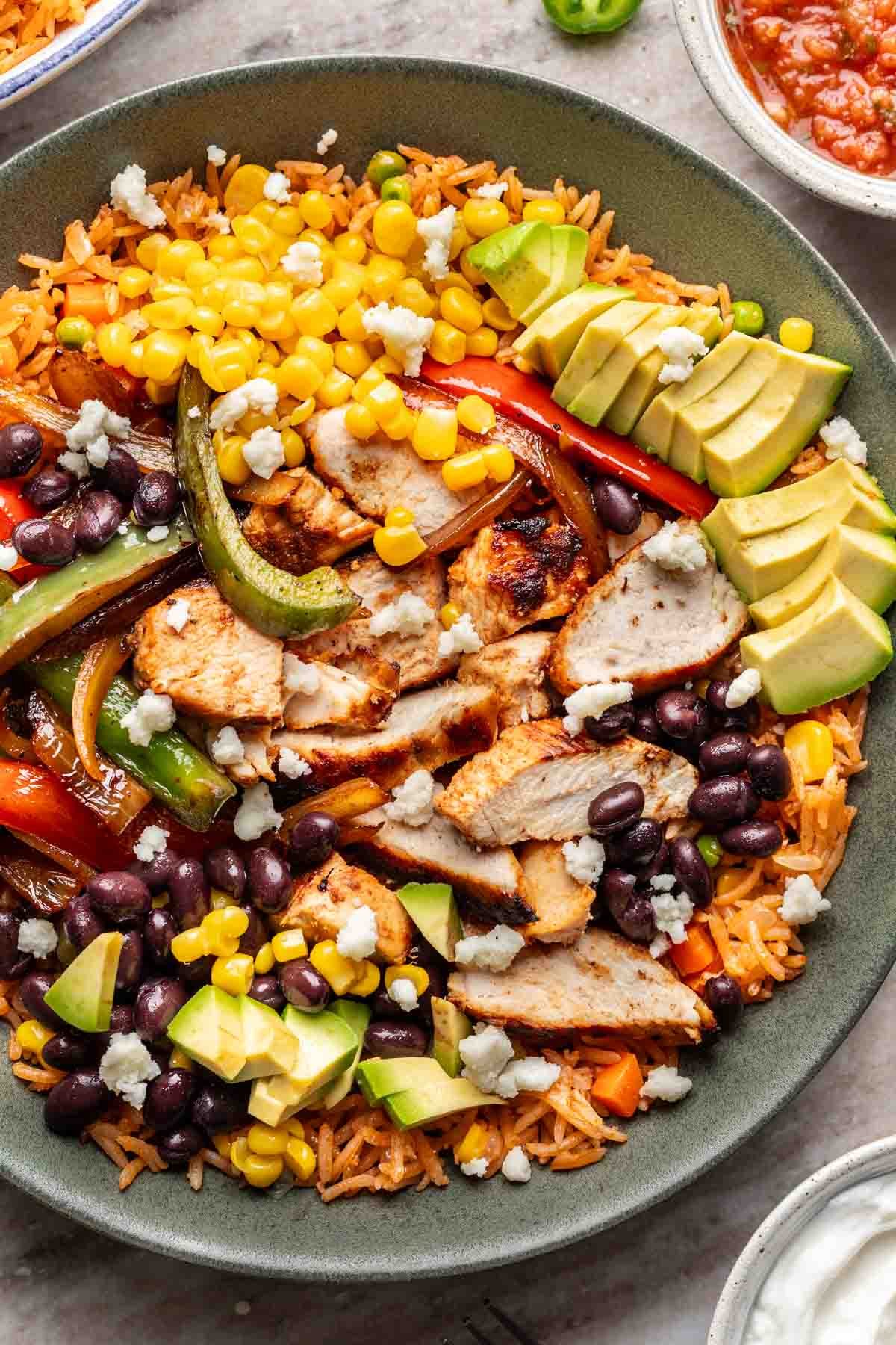 A chicken fajita bowl filled with rice, beans, corn, avocado, and other Mexican-inspired toppings.
