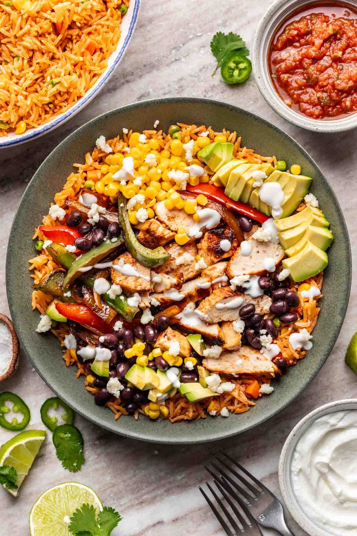 A chicken fajita bowl with mexican rice, salsa, and sour cream on the side.