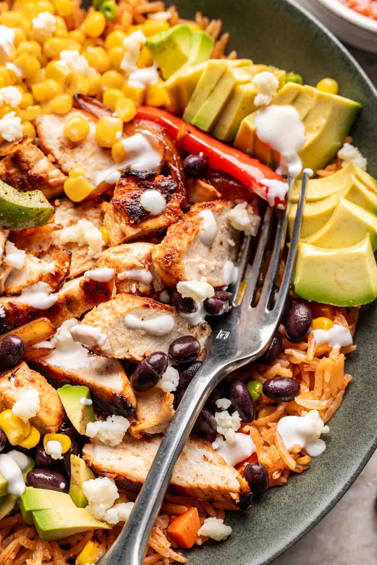 Fajita chicken, peppers, and onions on a bed of Mexican rice topped with avocado, sour cream, and other toppings.