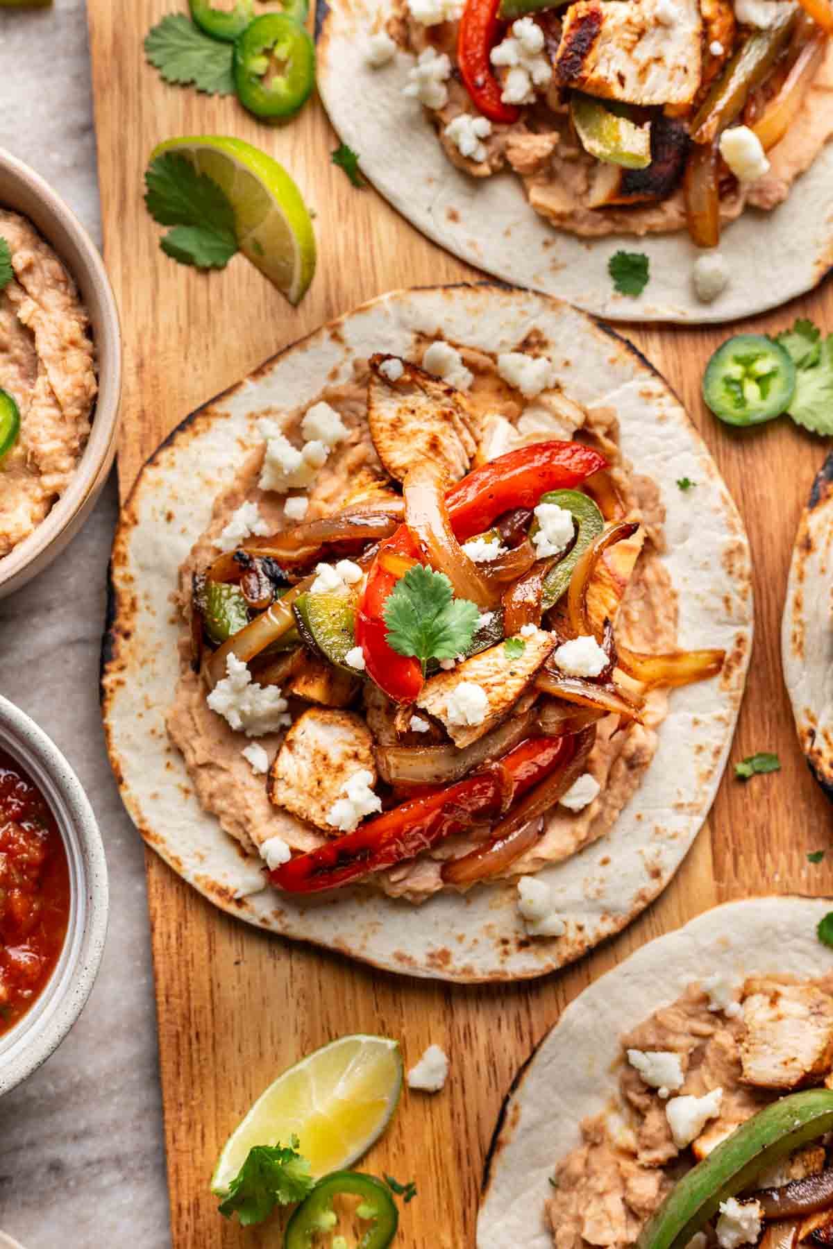 A chicken fajita taco piled high with all the toppings on a wood serving board.