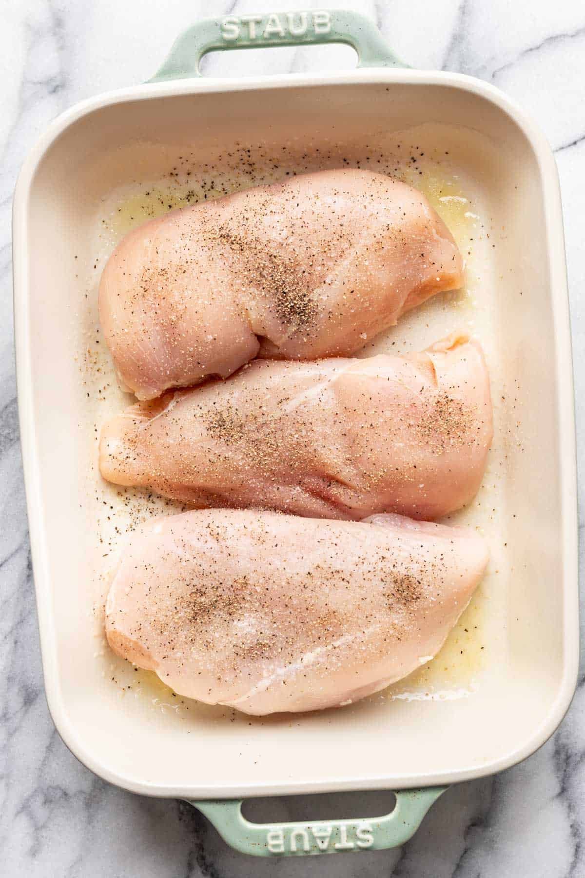Raw chicken in a baking dish seasoned with salt and pepper.