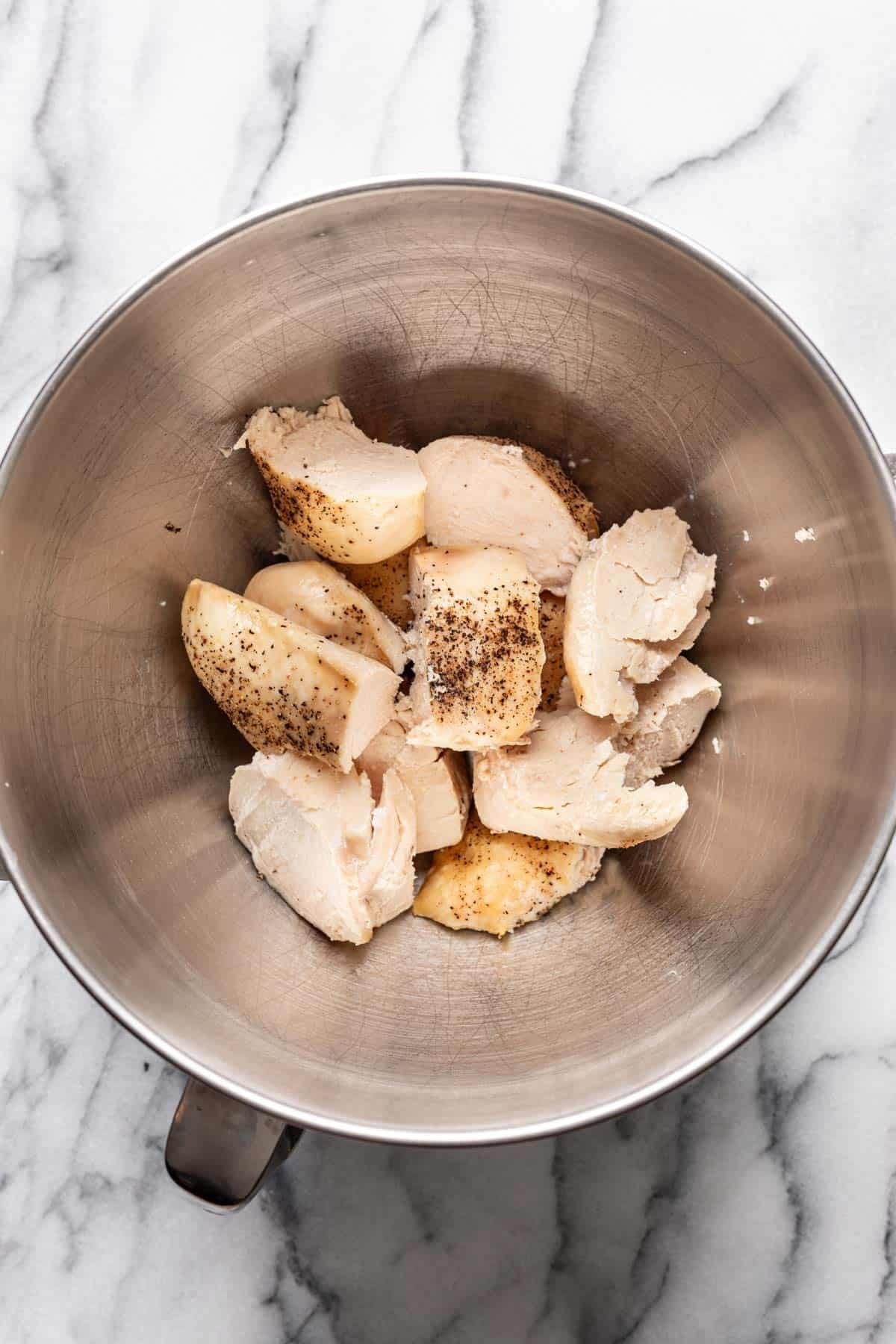 Cubed chicken in the bowl of a stand mixer.