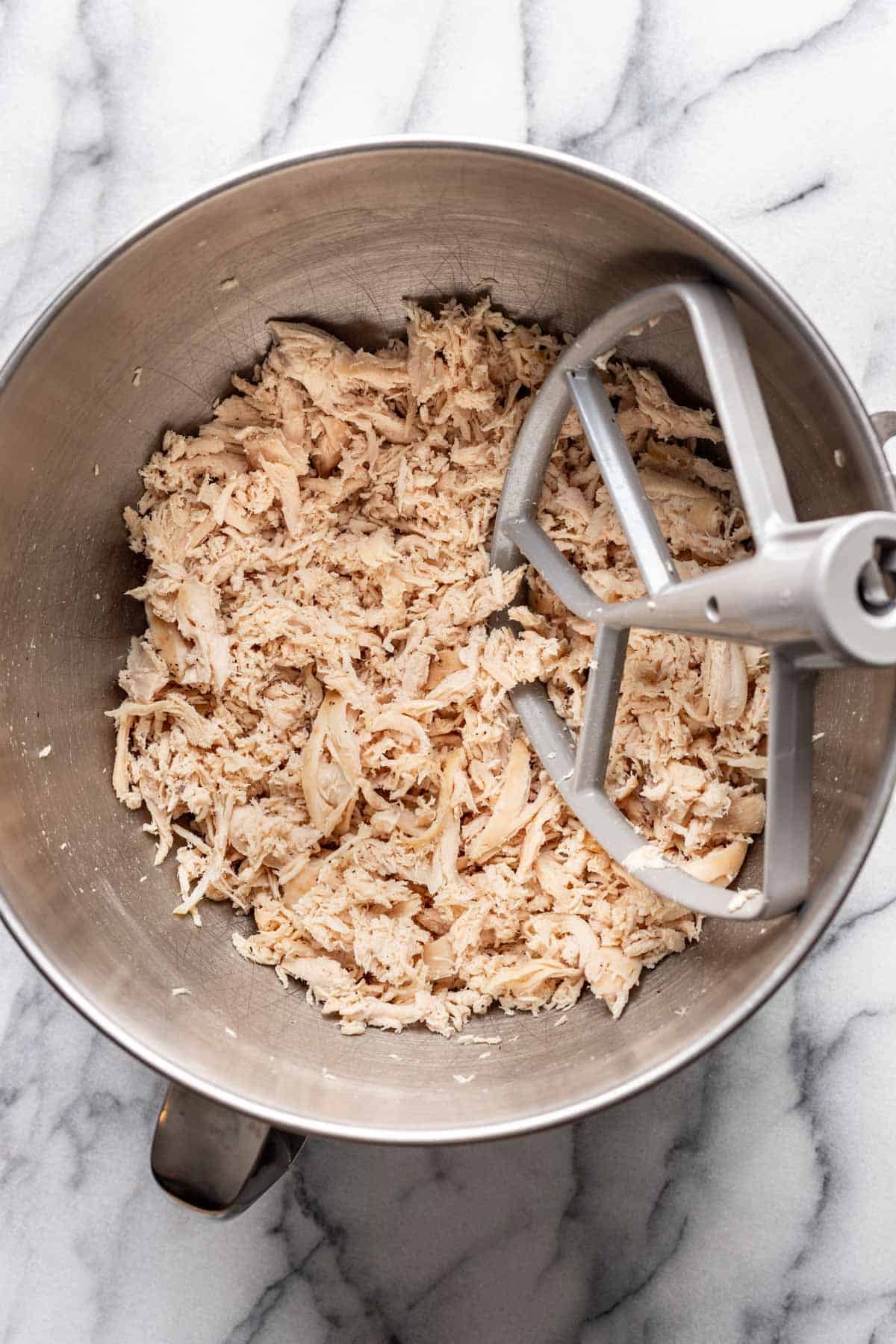 Shredded chicken in the bowl of a stand mixer.