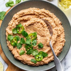 Homemade refried beans in a green bowl garnished with fresh cilantro.
