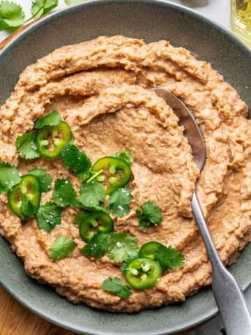 Homemade refried beans in a green bowl garnished with fresh cilantro.