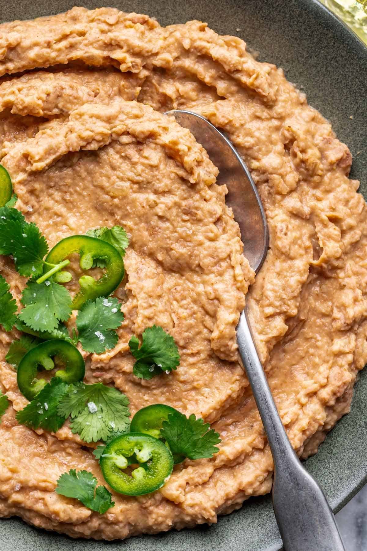 Homemade refried beans with a serving spoon and fresh cilantro.