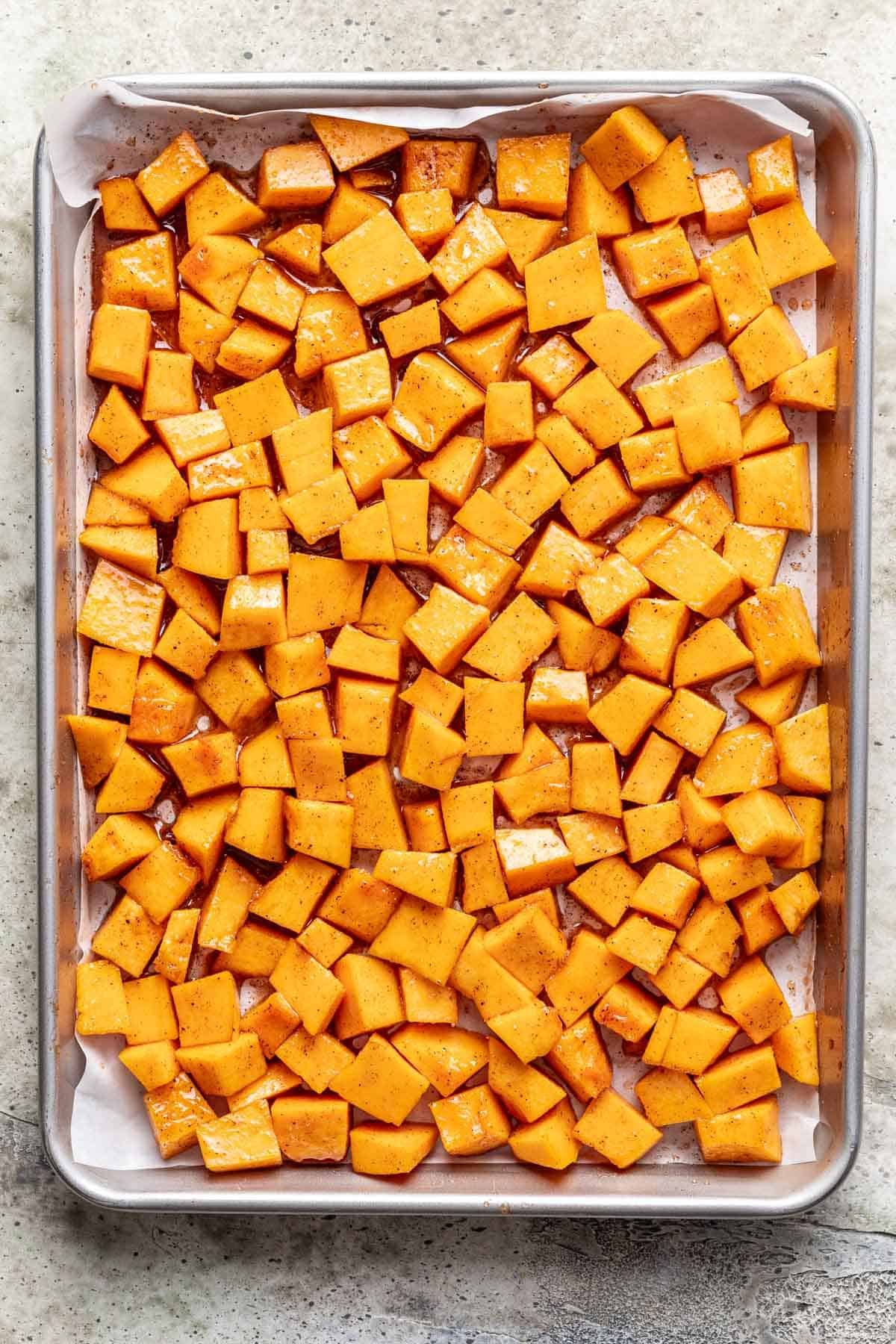 Cubed pumpkin on a lined baking sheet.