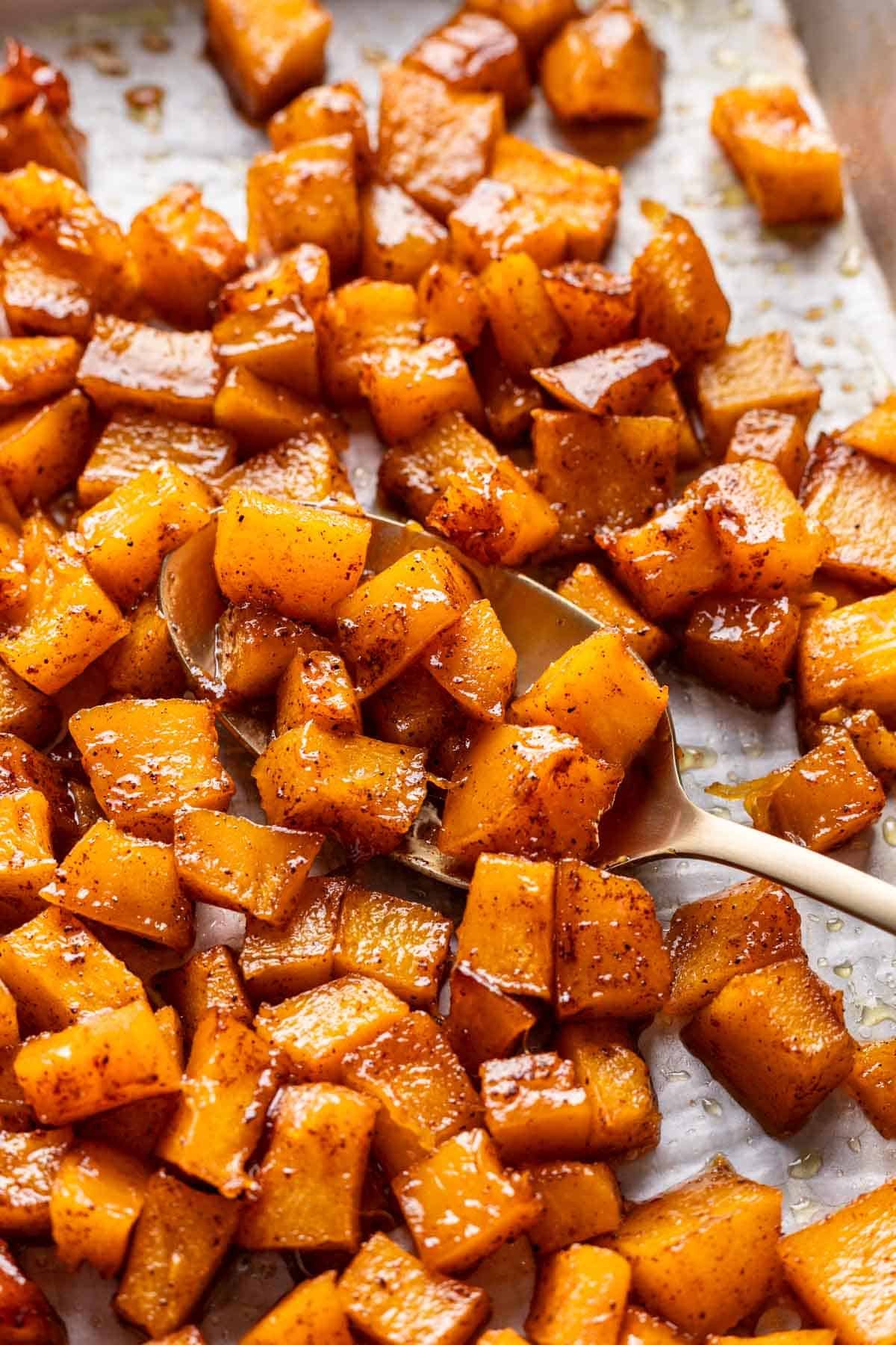 A serving spoon scooping maple brown sugar roasted pumpkin off a baking sheet.