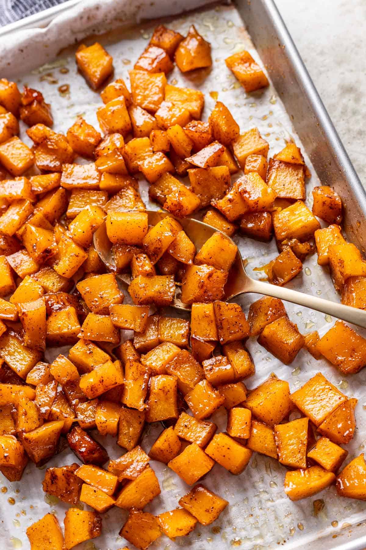 Maple brown sugar roasted pumpkin on a baking sheet with a serving spoon.