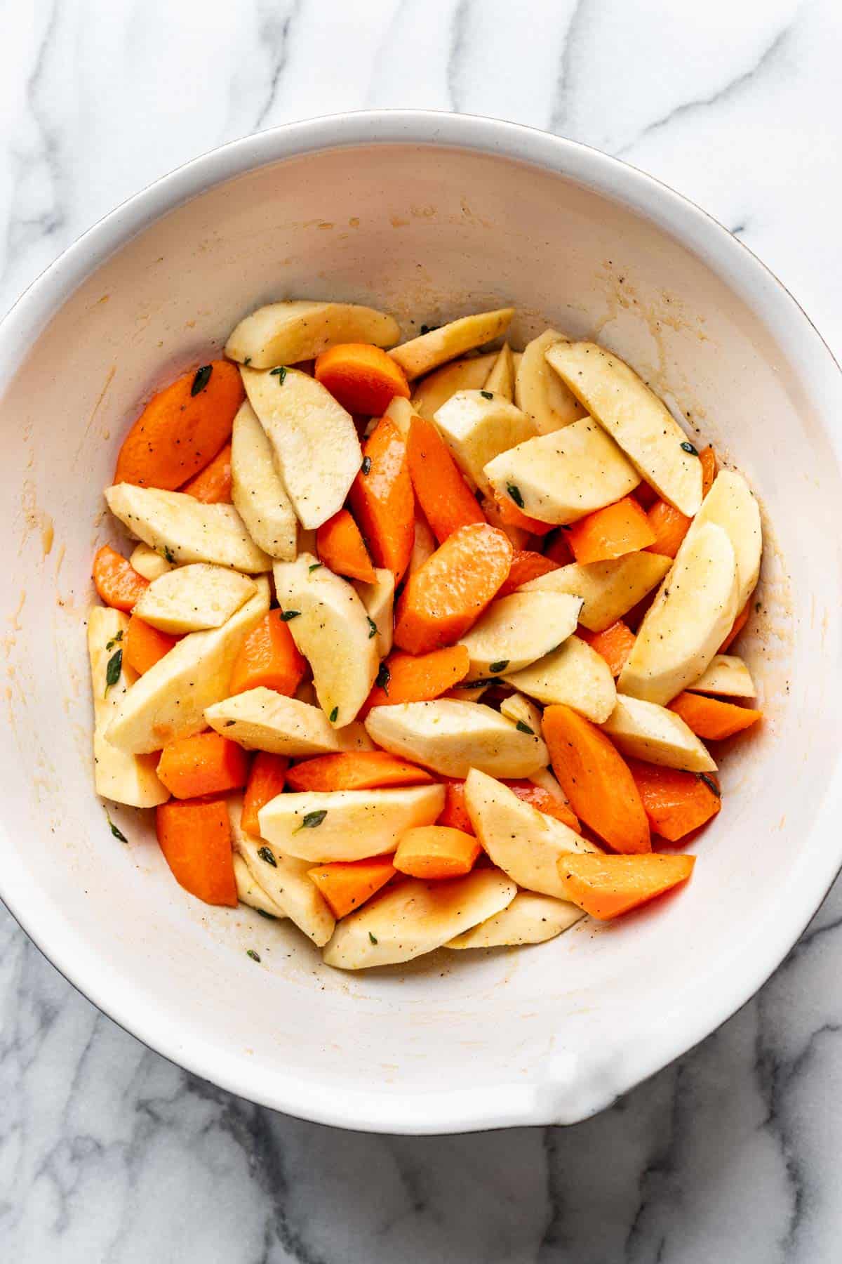 Carrots and parsnips mixed in the maple syrup and seasonings in a bowl.