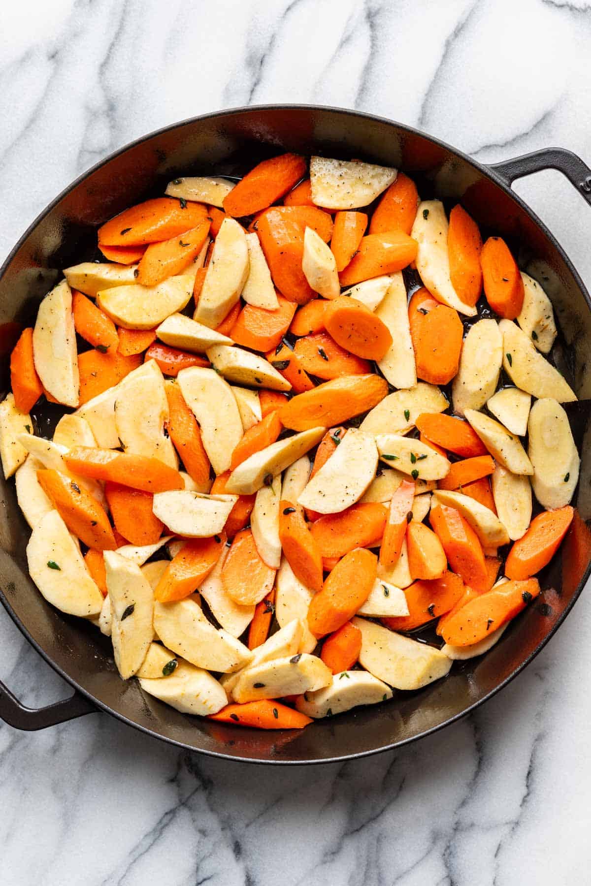 Seasoned carrots and parsnips in a roasting pan prior to roasting.