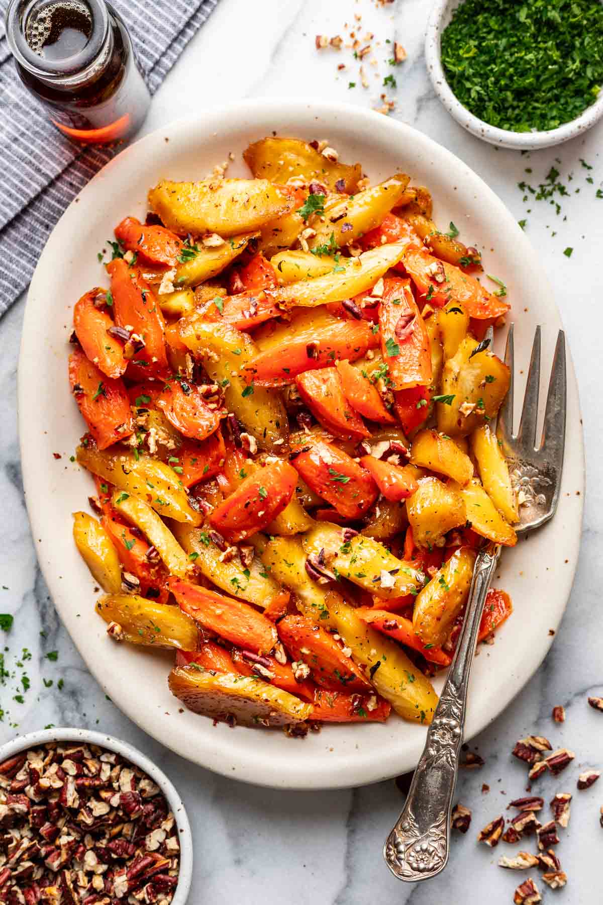 Maple roasted carrots and parsnips on a white serving platter, garnished with toasted pecans and fresh parsley.