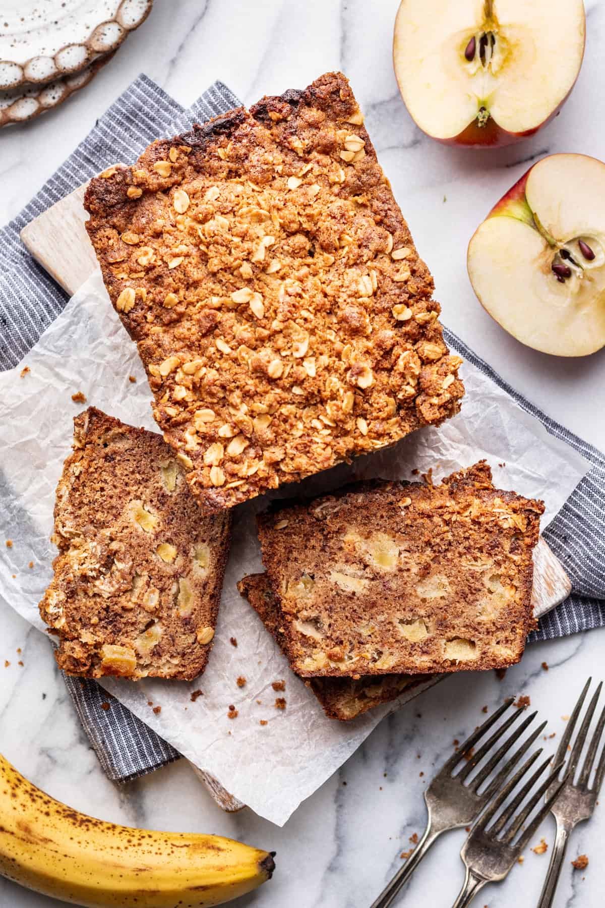 A loaf of apple banana bread on a wood platter with slices around it.