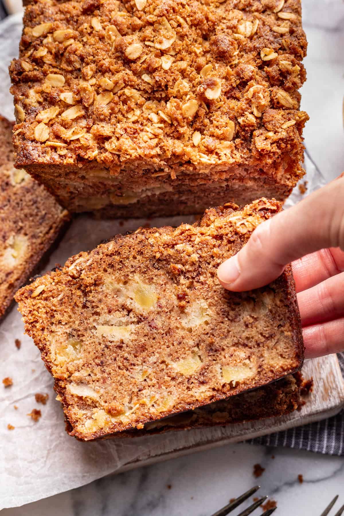 A hand grabbing a slice of apple banana bread.