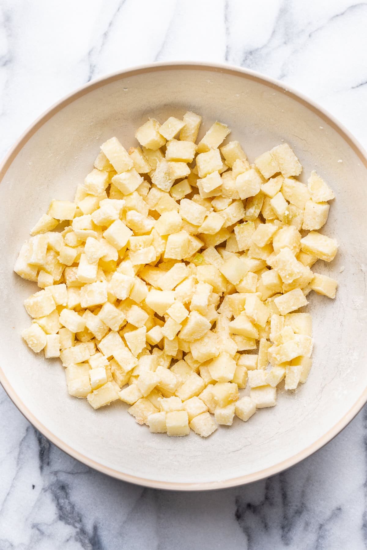 Apples coated in flour in a mixing bowl.
