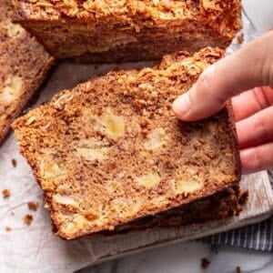 A hand picking up a slice of apple banana bread.