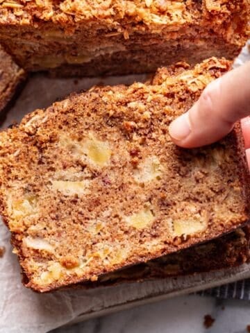 A hand picking up a slice of apple banana bread.