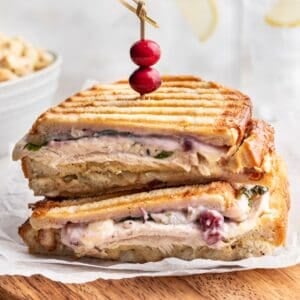 A panini sandwich filled with Thanksgiving leftovers on a wooden cutting board.