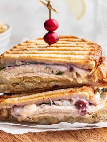 A panini sandwich filled with Thanksgiving leftovers on a wooden cutting board.