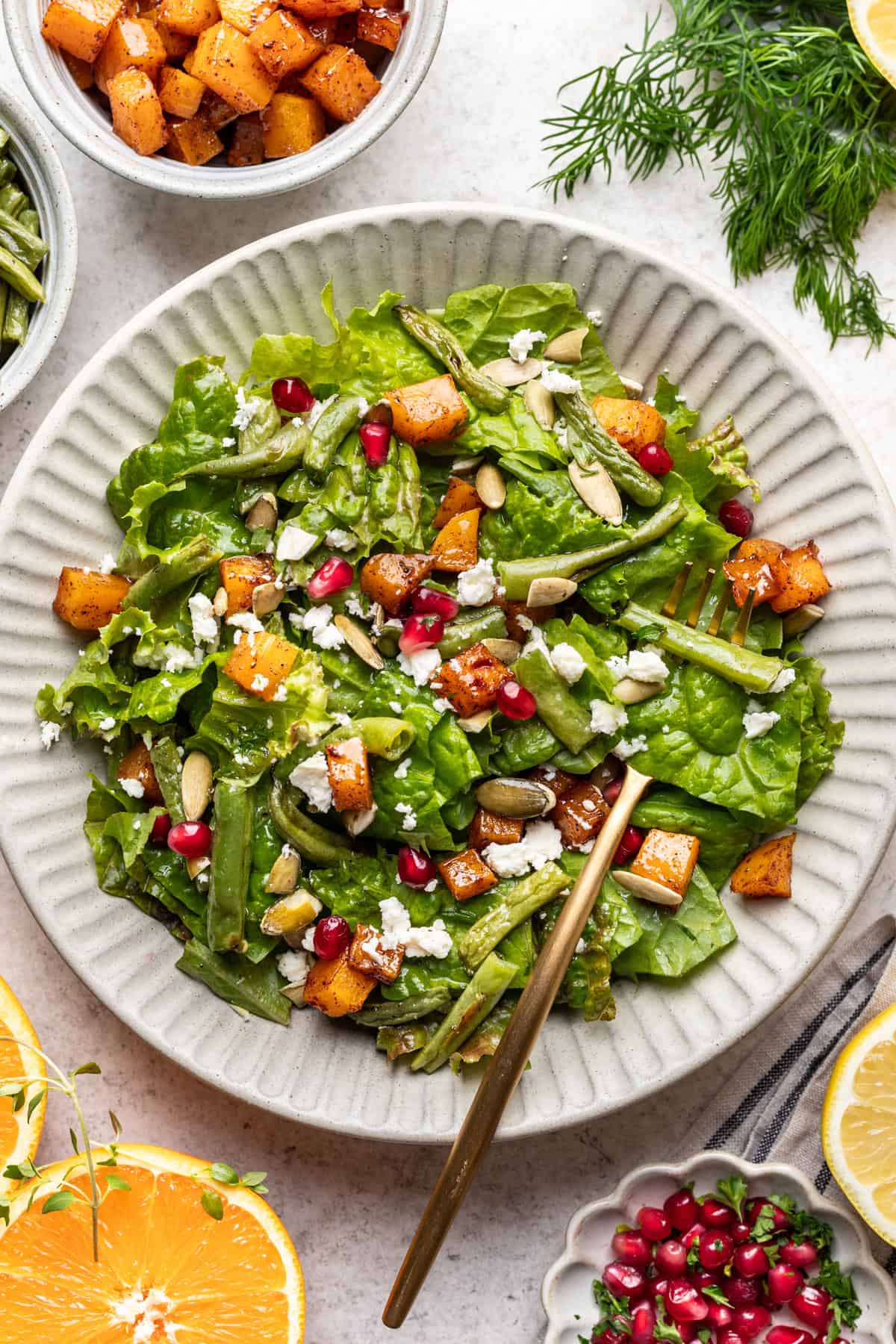 Roasted green bean and butternut squash salad in a bowl with pomegranate seeds, feta, and pepitas on top.