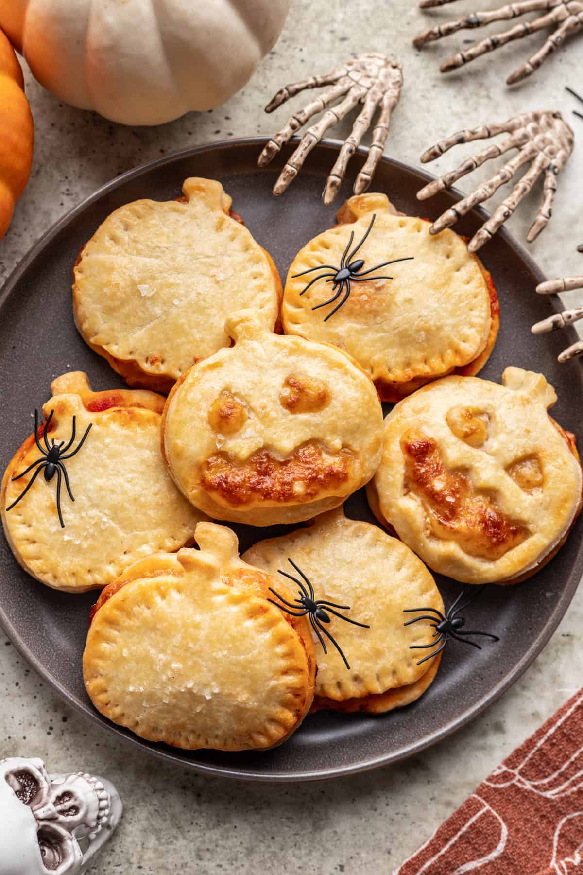 Jack o lantern pizza rolls stacked on a serving platter with halloween decor around it.