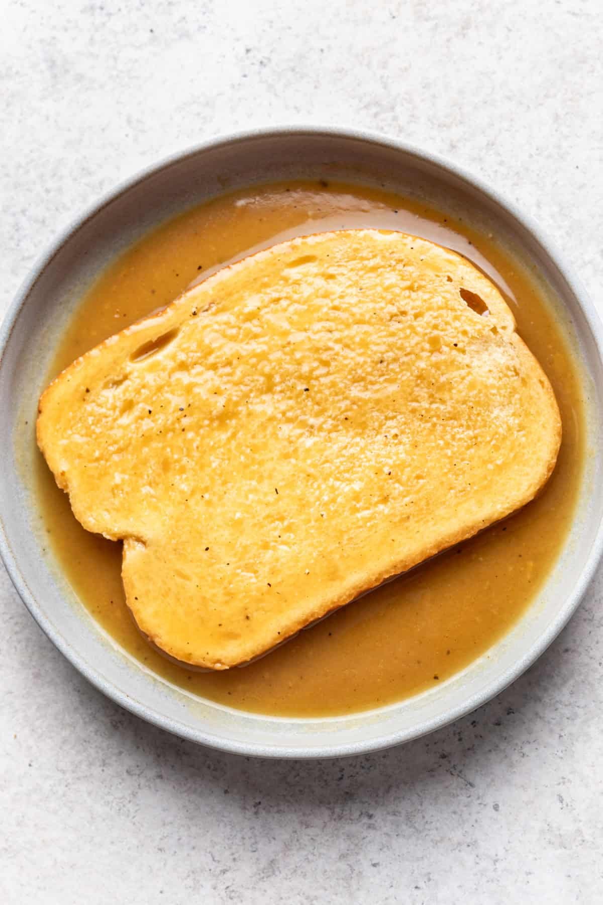 Gravy in a bowl with a slice of bread.