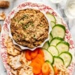 Vegetarian chopped liver in a serving bowl with cucumbers, carrots, and crackers on the side.